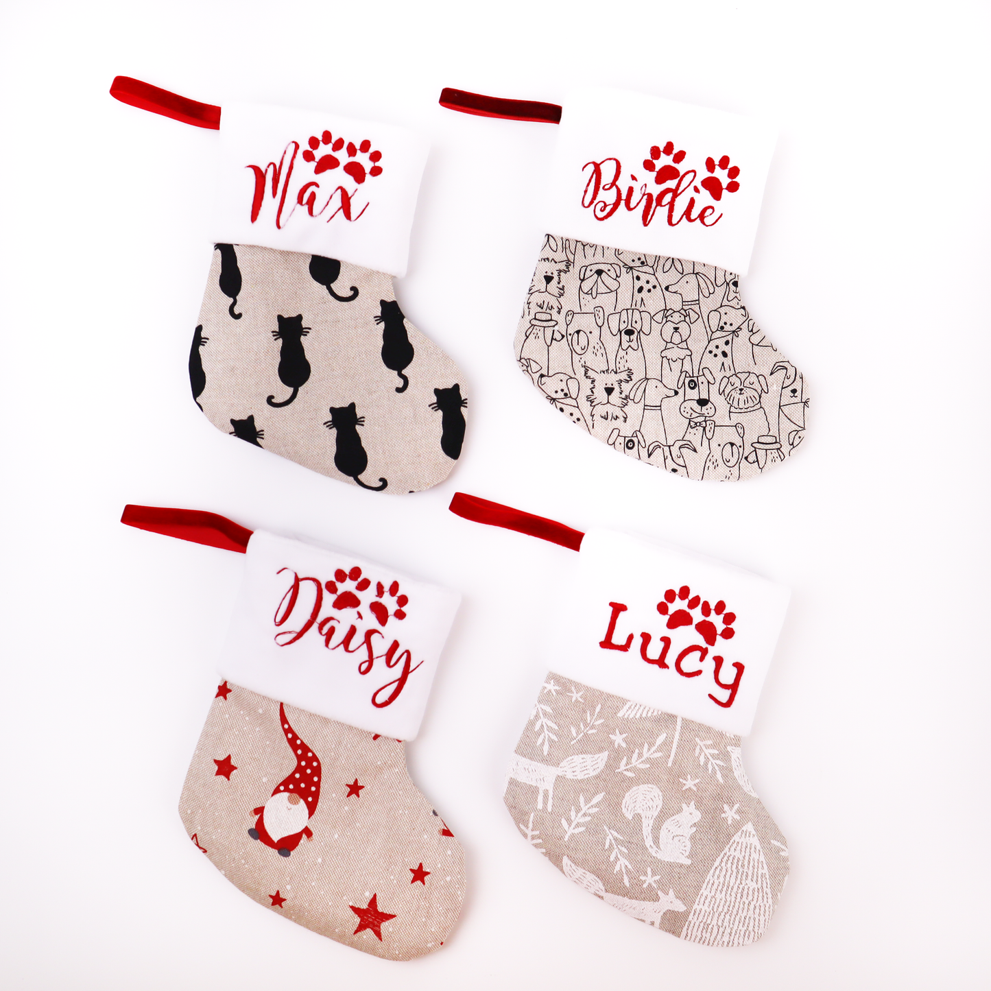 Four personalized Christmas stockings arranged in a 2x2 grid on a white background. Each stocking has a red fabric loop at the top, a white cuff with red embroidered name and paw print, and a printed fabric body.