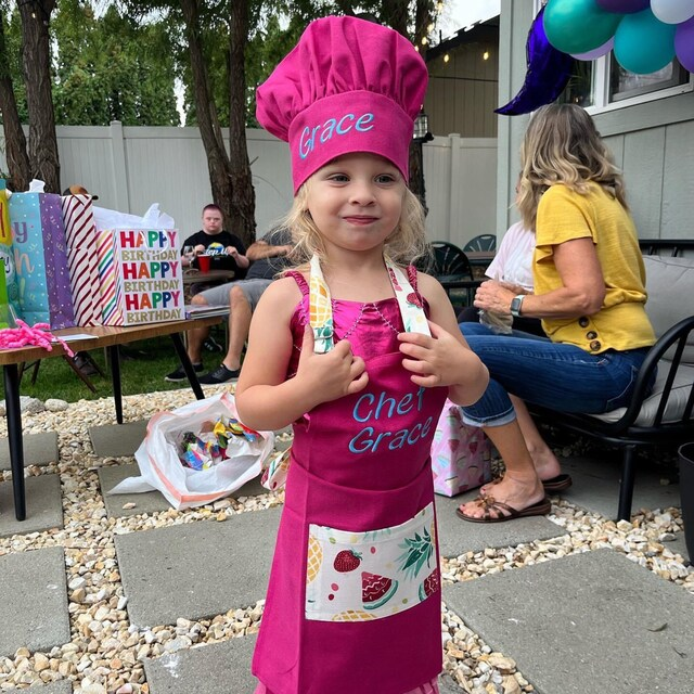 Little girl wearing personalized pink apron and chef hat with embroidered name Grace – kids birthday gift idea for girls
