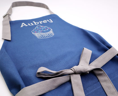 Close-up of the name "Aubrey" embroidered above a small icon on a personalized navy apron