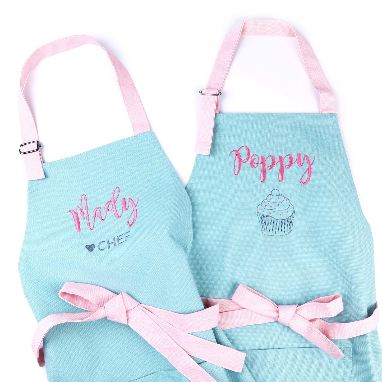 Two personalized light mint aprons with pink straps and bows, displayed on a white background. One apron is labeled 'Madly CHEF' and the other 'Poppy' with a cupcake illustration.