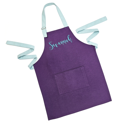 Personalized purple kids apron on a white background, straps untied, embroidered with the name "Savannah"