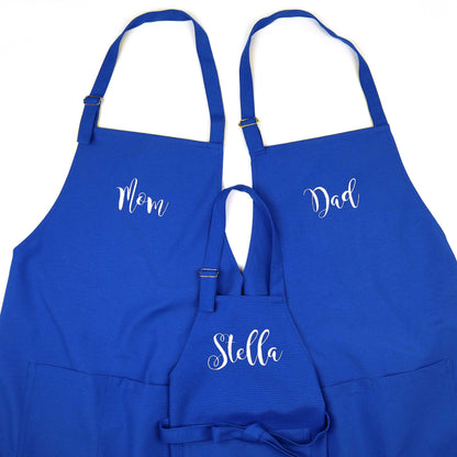 Three royal blue aprons with white script names 'Mom', 'Dad', and 'Stella' on a plain white background.
