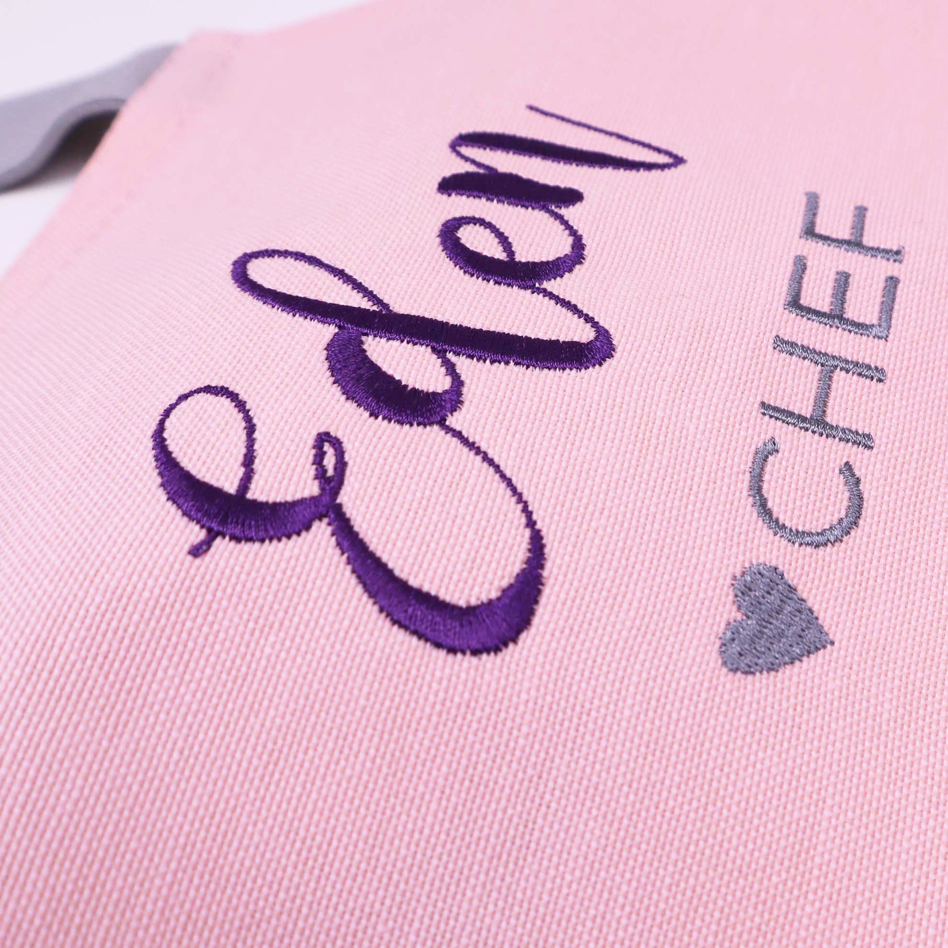 Close-up of a pink embroidered fabric item with the word "Eden" in purple script and "CHEF" in gray lettering next to a gray heart.