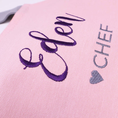 Close-up of a pink embroidered fabric item with the word "Eden" in purple script and "CHEF" in gray lettering next to a gray heart.