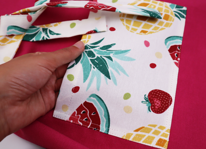 Close-up of a hand holding the strawberry and pineapple print fabric used for the apron trim