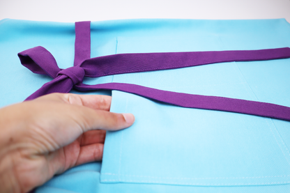 Close-up of a hand adjusting the purple strap on a personalized blue apron