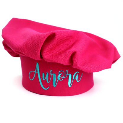 Personalized hot pink chef hat embroidered with the name "Aurora" in teal script