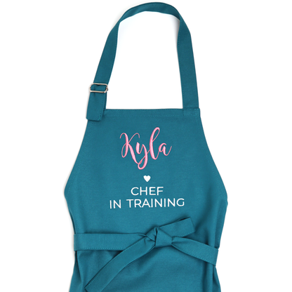 Personalized teal apron on a white background, embroidered "Kyla ♥ Chef in Training"