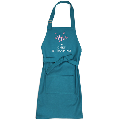 Personalized teal apron laid flat with straps untied, embroidered "Kyla ♥ Chef in Training"