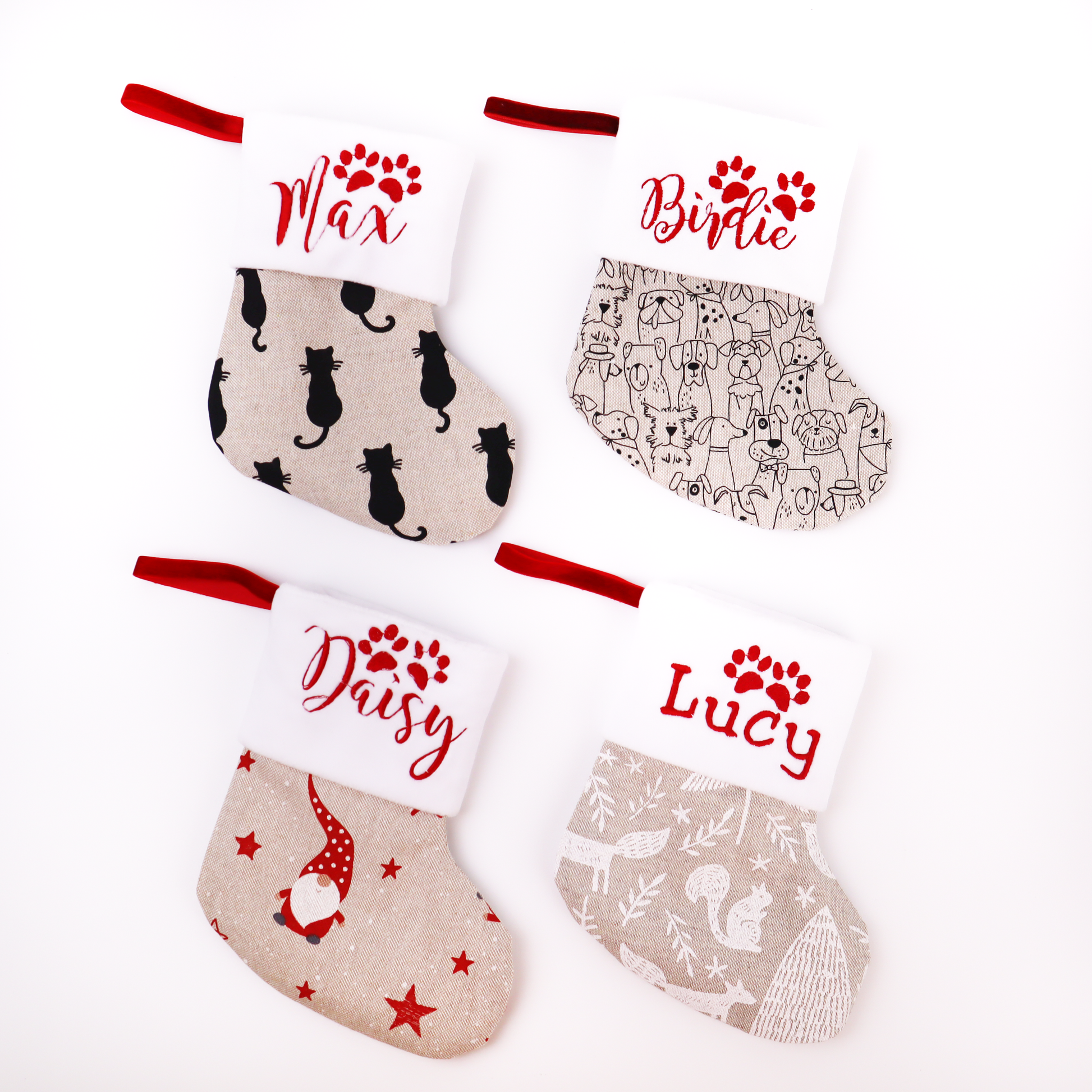 Four personalized Christmas stockings arranged in a 2x2 grid on a white background. Each stocking has a red fabric loop at the top, a white cuff with red embroidered name and paw print, and a printed fabric body.