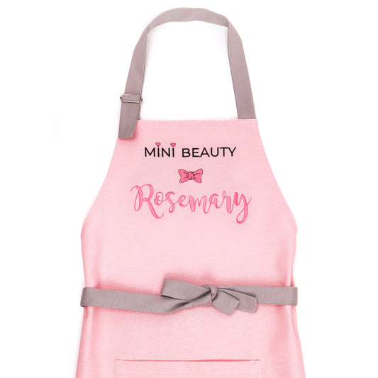 Personalized pink Mini Beauty apron for girls with embroidered name and bow — handmade in Minnesota