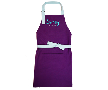 Personalized purple apron laid flat with straps spread out, embroidered with the name "Savannah"