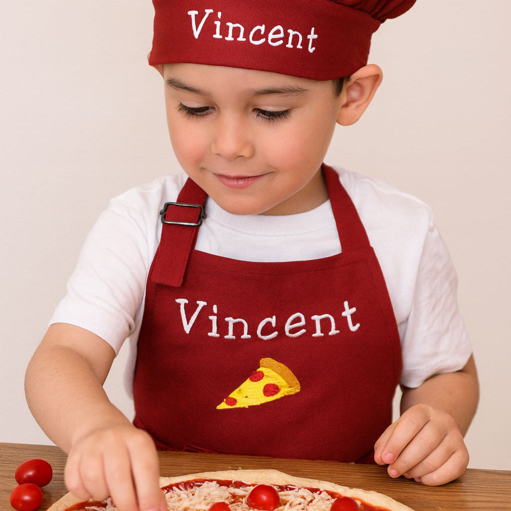 Child wearing a red chef's hat and apron with 'Vincent' embroidered, making a pizza.