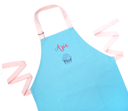 Personalized blue apron with straps untied, embroidered with the name "Aria" above a small icon