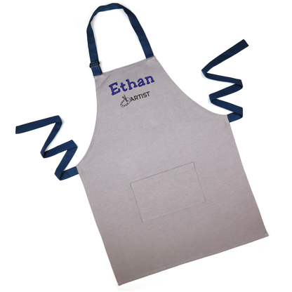 Personalized grey apron with navy straps spread out, embroidered with the name "Ethan"