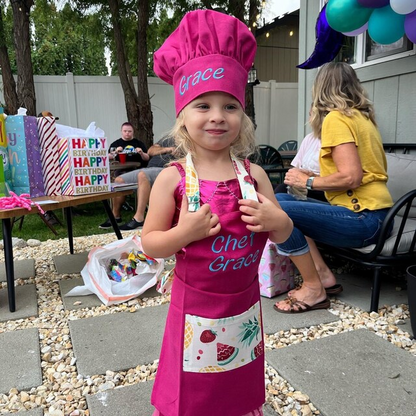 Little girl wearing personalized pink apron and chef hat with embroidered name Grace – kids birthday gift idea for girls
