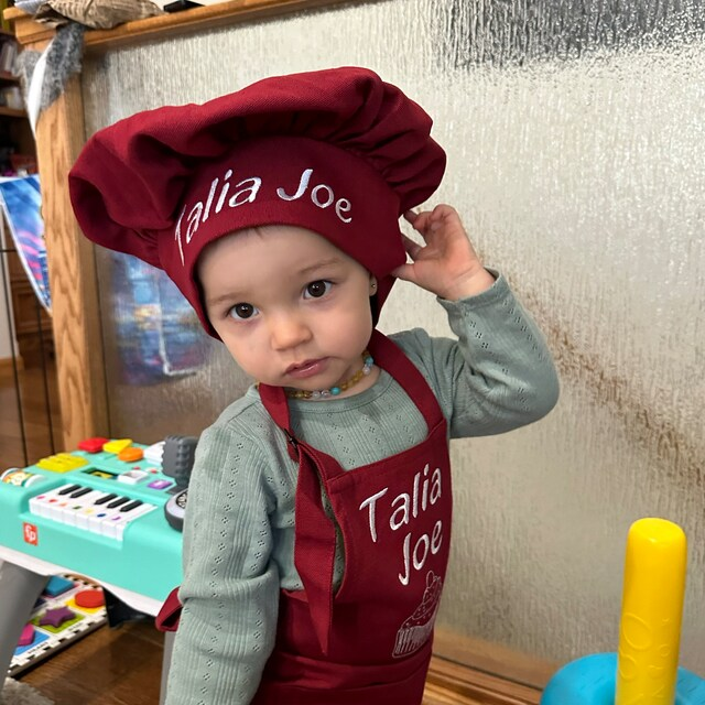 Toddler girl wearing personalized red apron and chef hat with embroidered name – custom kitchen gift for baby
