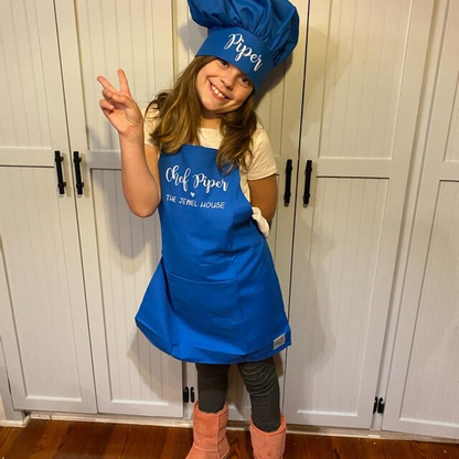 Child wearing a personalized royal blue apron indoors, making a peace sign