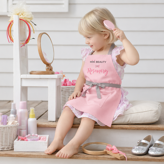 Little girl wearing personalized pink Mini Beauty apron playing salon — custom name kids gift