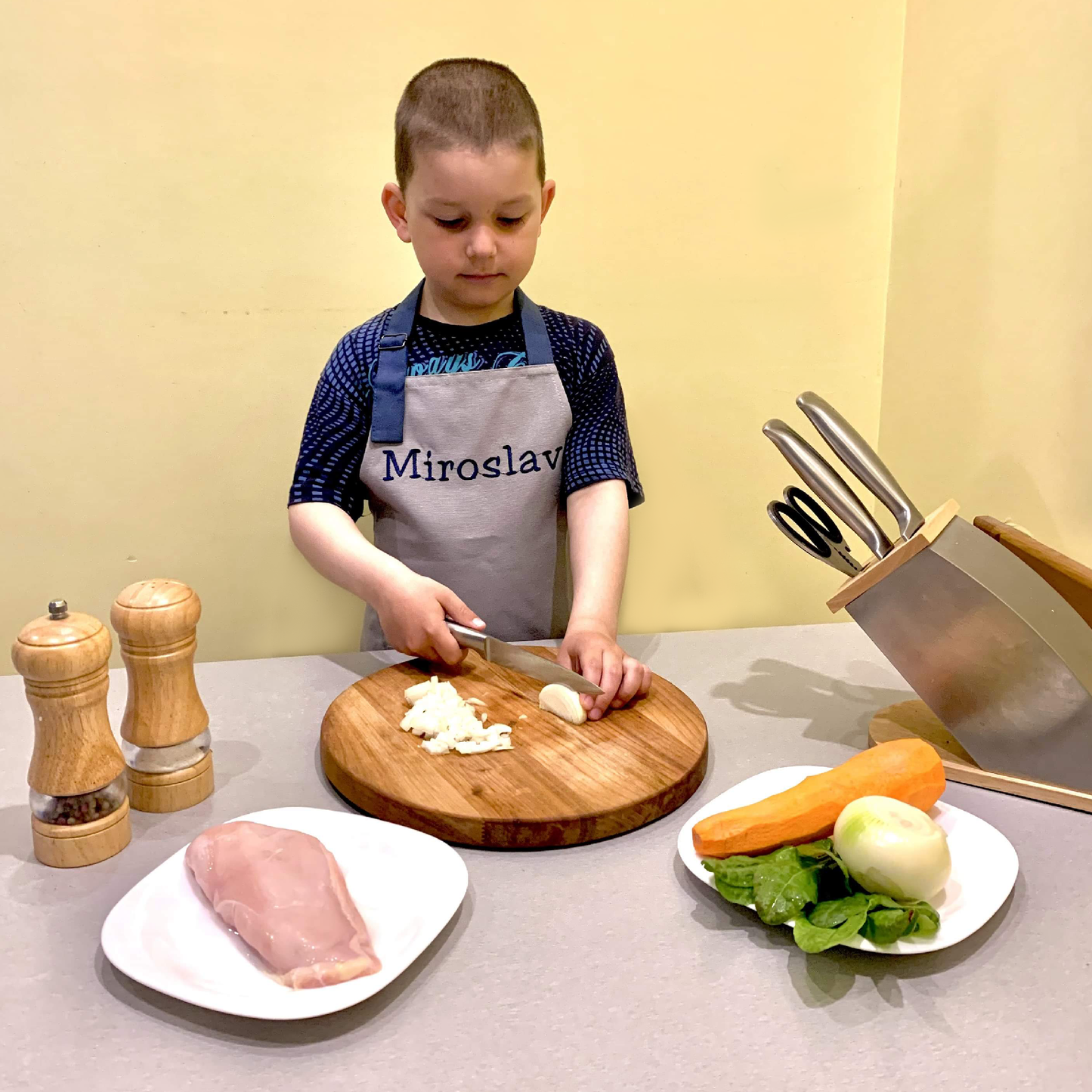 Boy wearing personalized gray apron with name, chopping onions – custom kids chef apron